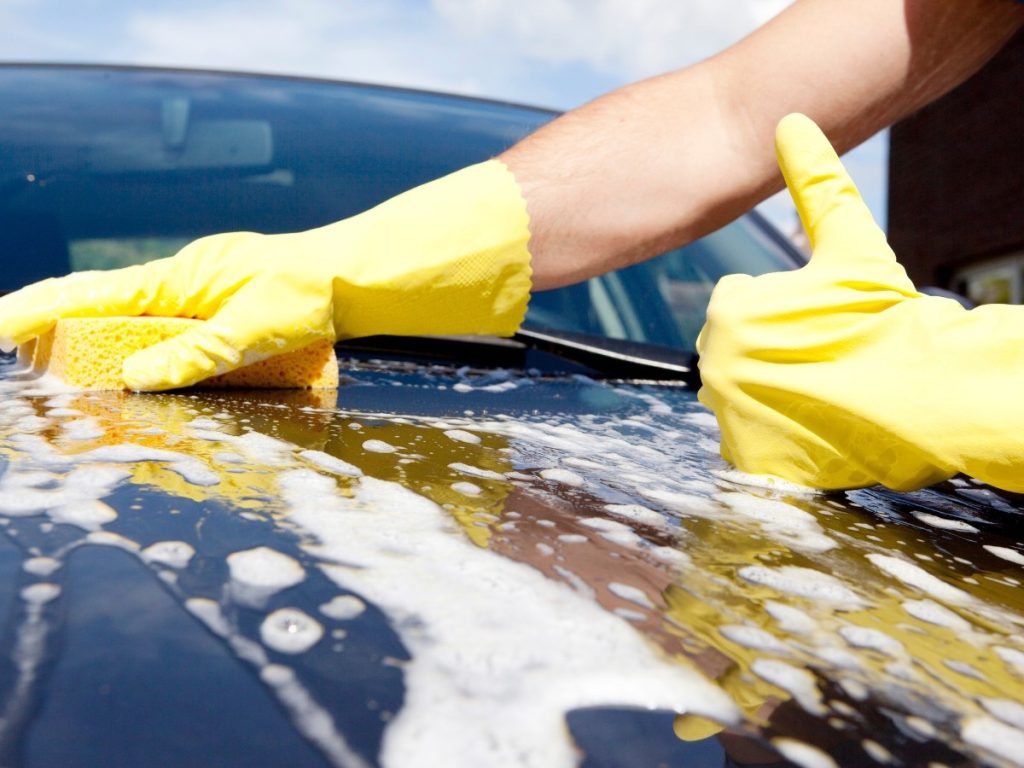 Detail of a person using a sponge to clean a car's paint in an Affordable monthly membership car wash in Kelliwood