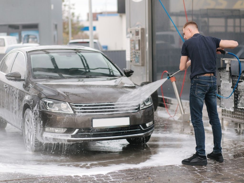 Man washing a car with a high-pressure hose at a self-service bay, illustrating the Best Car Wash Loyalty program in Cinco Ranch Equestrian Village.