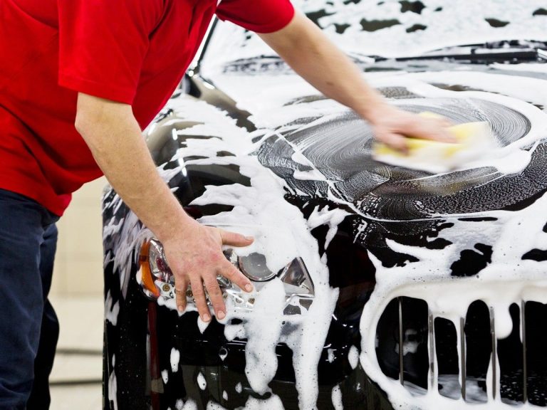 Car Wash Loyalty Program in Katy TX, a person's hands washing the hood of a black car with soapy foam.