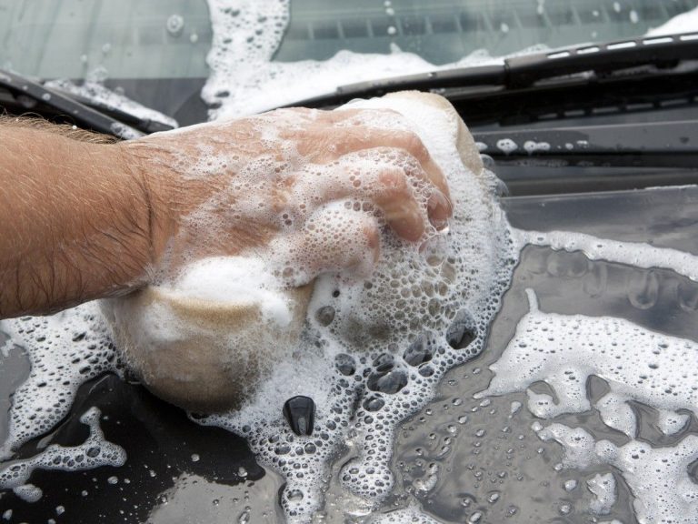 Car Wash Membership in Katy TX, a close-up of a hand scrubbing the soapy hood of a car with a wash mitt.