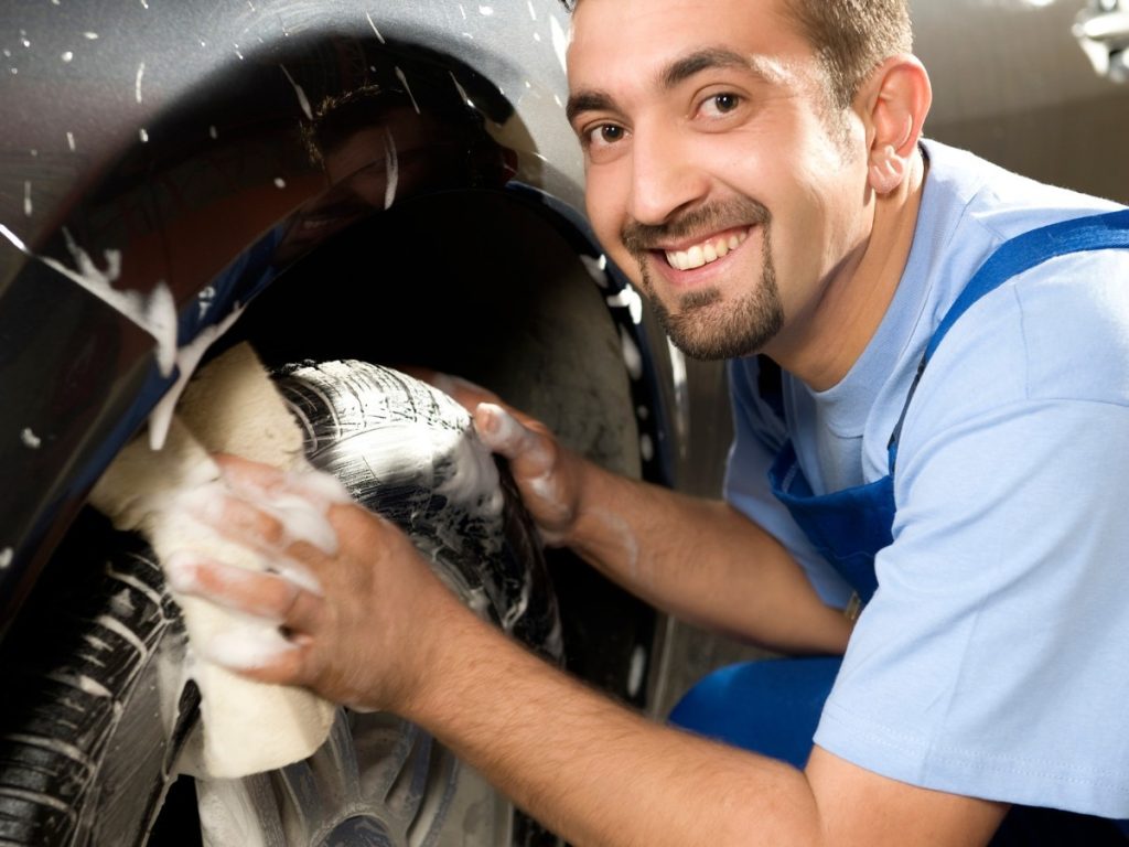 Car wash membership offers in Kelliwood Park, a friendly employee smiling while washing the side of a car by hand with a wash mitt.