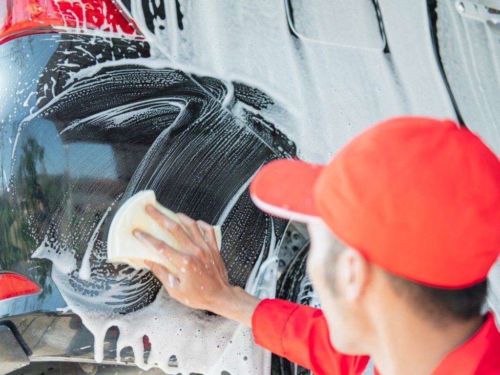 Close-up of a person's hand scrubbing a vehicle with a sponge and soapy foam, demonstrating the value you get with discount car wash plans in Kelliwood Park
