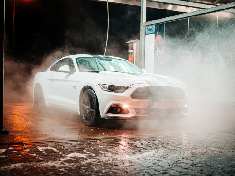 A shiny white sports car being rinsed with water and steam at a self-service bay, showing the kind of wash you can get with a monthly car wash subscription in Katy TX