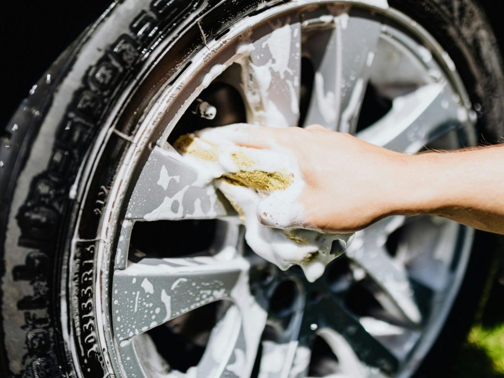 Hand cleaning car wheel with soapy sponge at Best Car Wash Membership Katy TX.