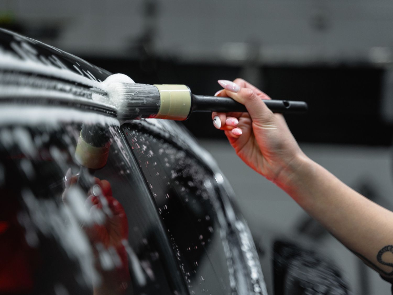 Hand using foam brush to clean wet car window at Drive-Thru Car Wash Katy TX.