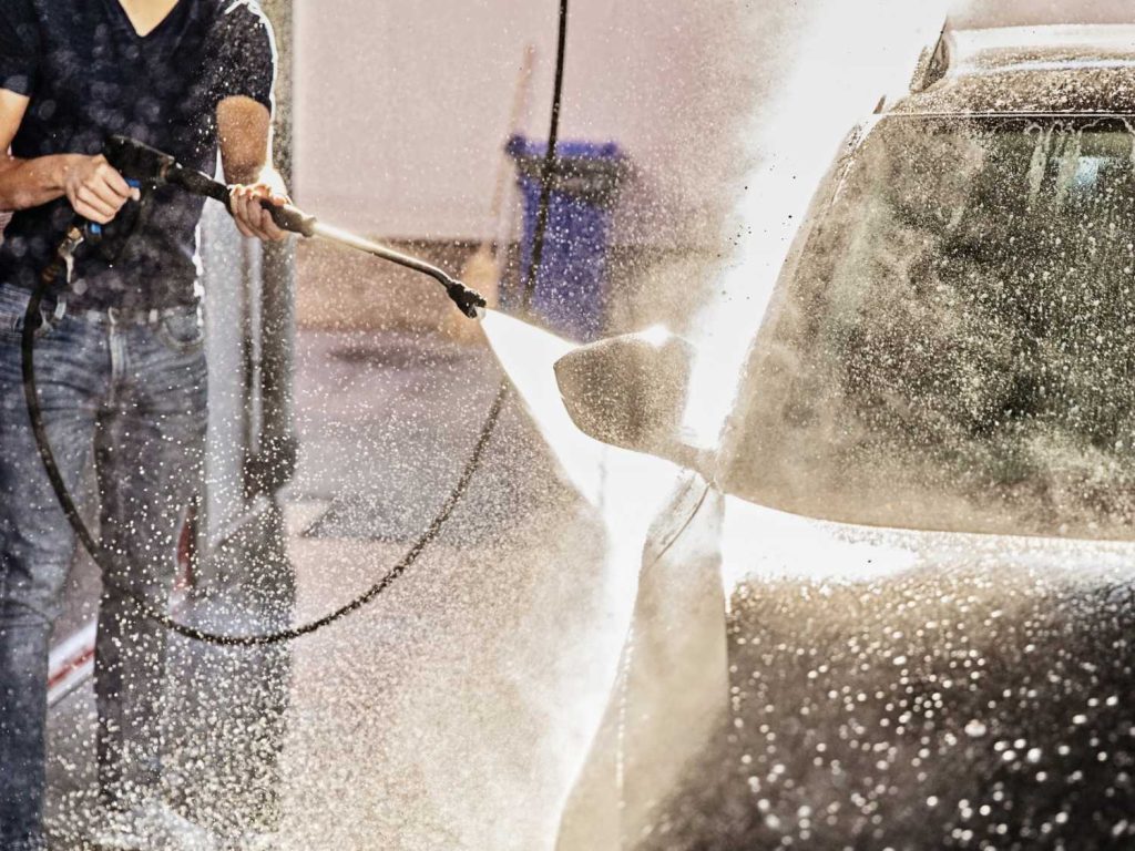 Drive-Thru Car Wash Katy TX — worker pressure-washing a car as water sprays and droplets cover the vehicle.
