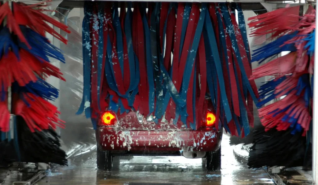 Red car getting scrubbed by blue and red brushes inside the automatic tunnel for the Best Car Wash in Katy TX.