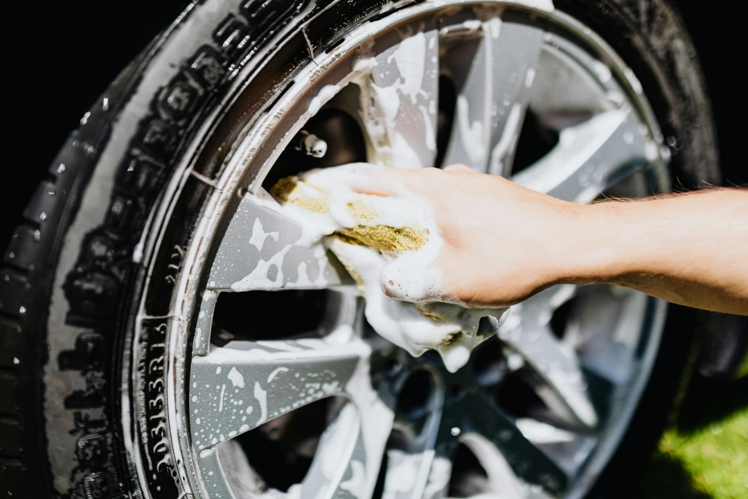Hand scrubbing car wheel rim with a sponge and soap, showing detail work at an Affordable Car Wash Katy TX.