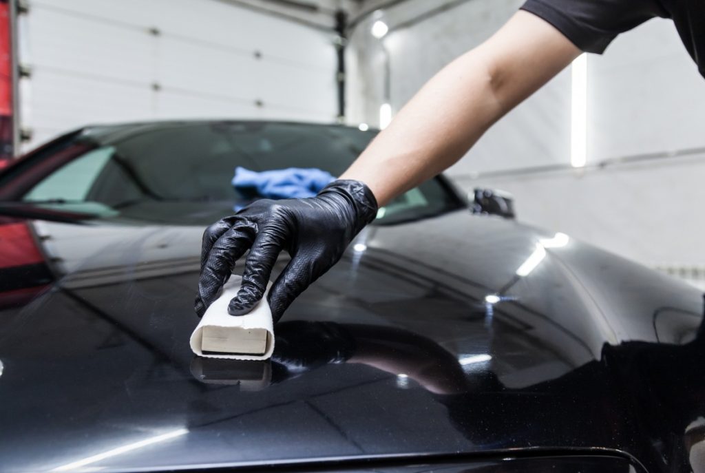 Professional applying long-lasting ceramic coating to a black vehicle. Visit the Best Car Wash in Katy TX for superior finish.