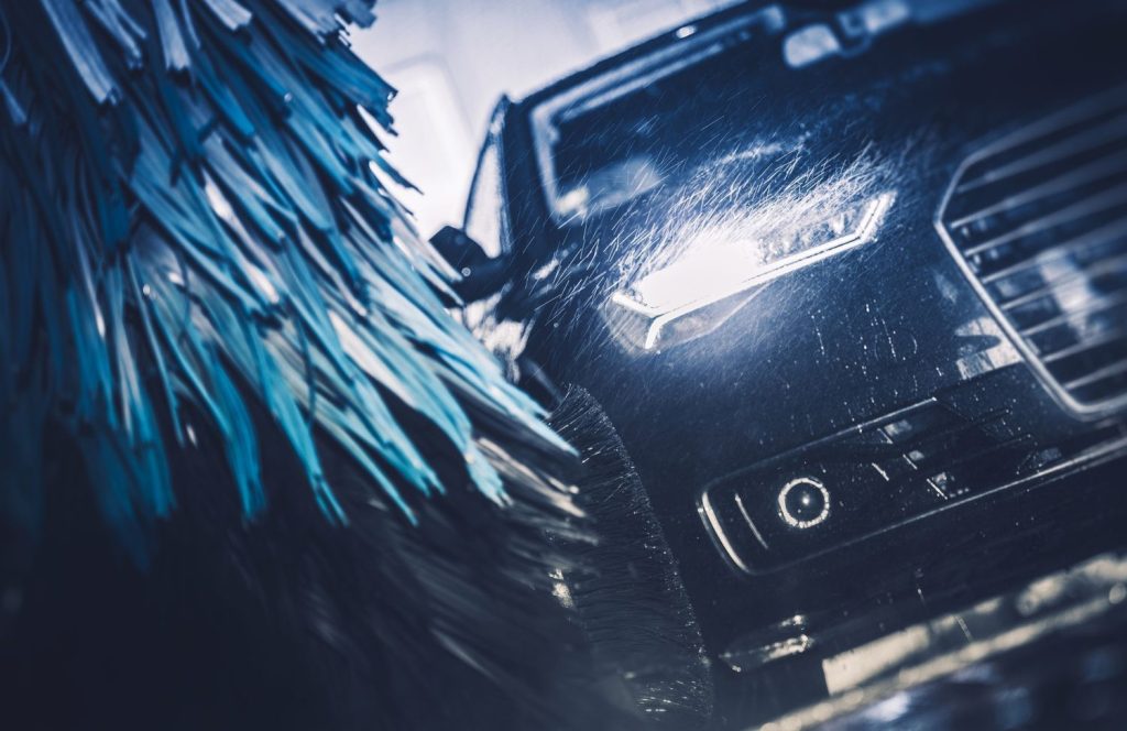 Brightly lit headlights of a car passing through the deep cleaning blue brush at a drive-thru car wash in Katy TX.