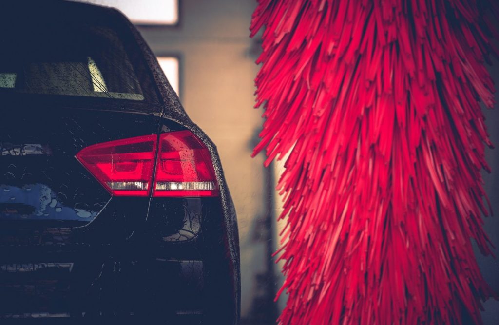 The rear of a clean black vehicle next to the large red spinning brush inside a drive-thru car wash in Katy TX.
