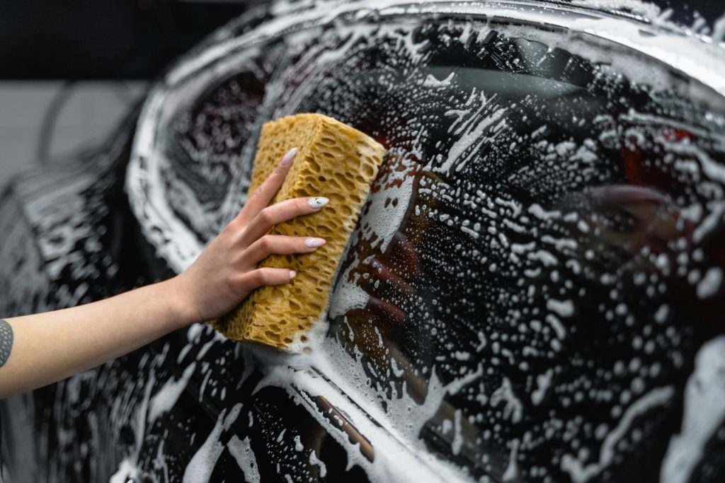 Close-up of hand with sponge thoroughly scrubbing a car surface for a cheap car wash Katy TX.