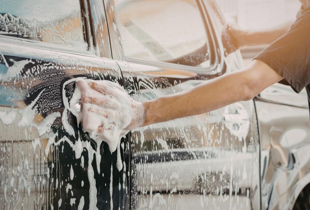 Person's hand washes the car door handle area with rich soap at a cheap car wash Katy TX.
